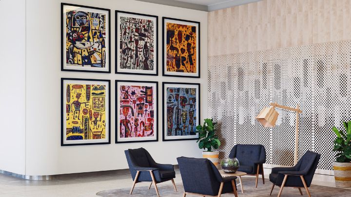A hotel lobby with six colourful paintings on the wall and lounge chairs in the centre
